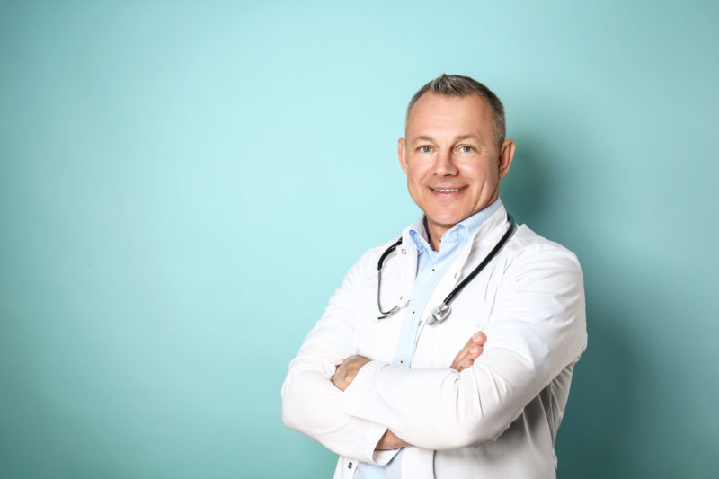 Handsome middle-aged doctor on color background